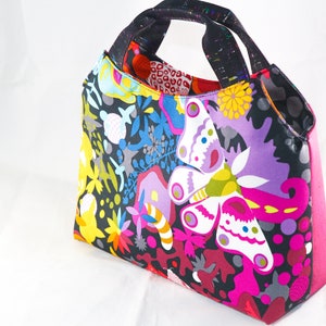 May include: A colorful tote bag with a black background and a butterfly design. The bag has a pink lining and two black handles.
