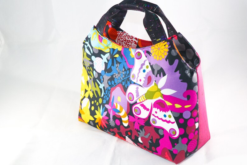 May include: A colorful tote bag with a black background and a butterfly design. The bag has a pink lining and two black handles.