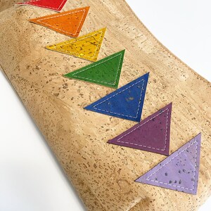 May include: A cork clutch with a rainbow of colorful triangle accents. The triangles are red, orange, yellow, green, blue, purple, and lavender, each with white stitching. The bag has a metal clasp and a strap.