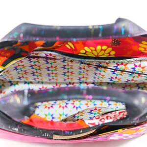 May include: A black and pink tote bag with a colorful floral print and a zippered top. The bag has a white lining with a star pattern.