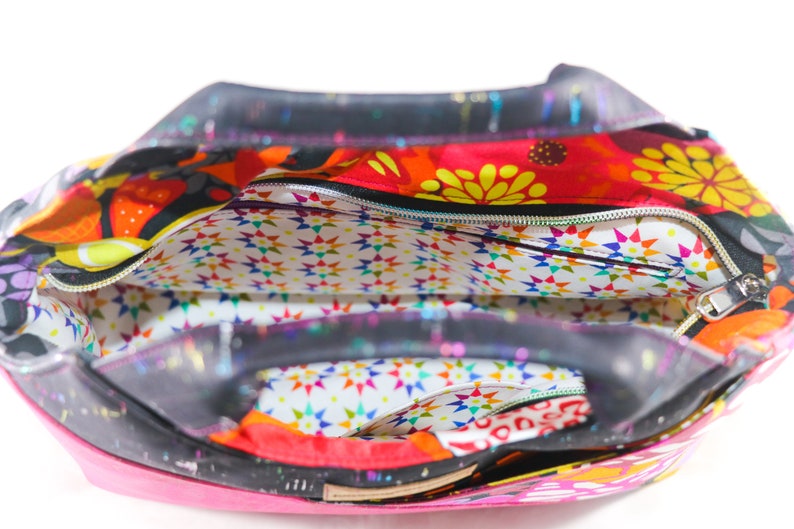 May include: A black and pink tote bag with a colorful floral print and a zippered top. The bag has a white lining with a star pattern.