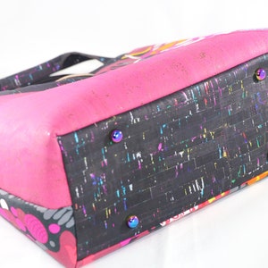 May include: A black and pink tote bag with a colorful cork bottom. The bag has a zipper closure and four metal studs on the bottom.