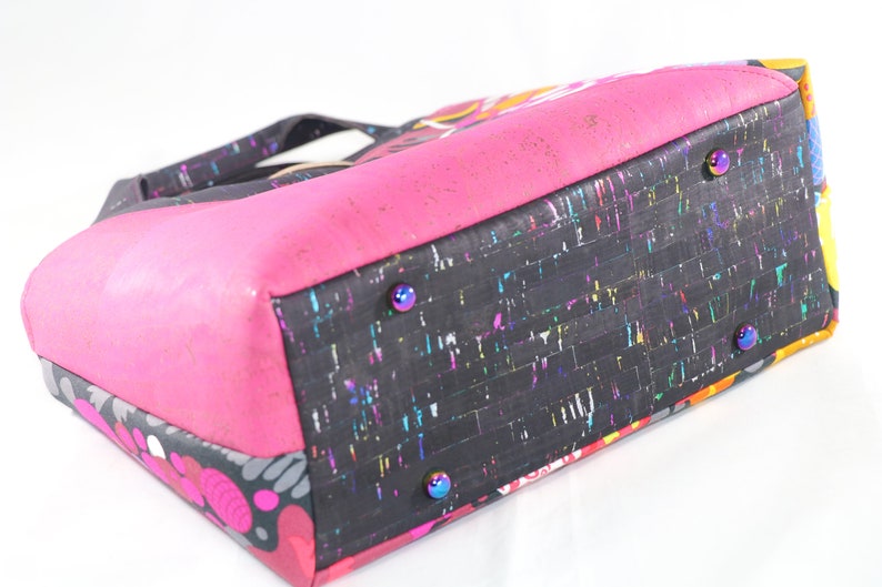 May include: A black and pink tote bag with a colorful cork bottom. The bag has a zipper closure and four metal studs on the bottom.