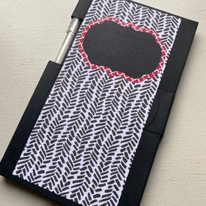 Könnte beinhalten: Schwarzes Notizbuch mit einem schwarz-weißen Chevron-Muster und einem schwarzen Etikett mit rotem Rand. Das Etikett hat einen leeren Platz zum Schreiben.