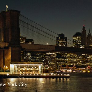 Puede incluir: Una vista nocturna del puente de Brooklyn con el horizonte de la ciudad de Nueva York al fondo. El puente está iluminado con luces, y el horizonte de la ciudad también está iluminado. La imagen se tomó desde el lado de Brooklyn del puente, mirando hacia Manhattan.