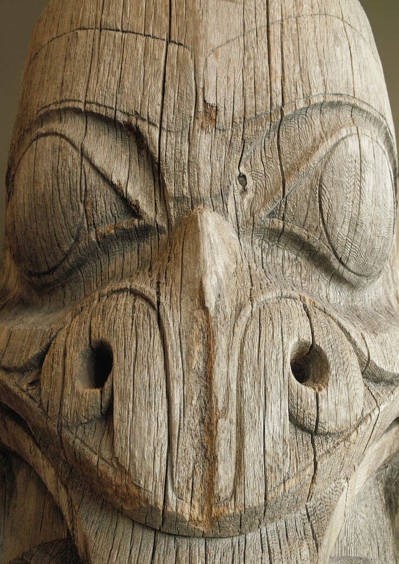 May include: Close-up of a wooden carving of a face with a wide mouth and large eyes. The carving is weathered and has a rough texture.