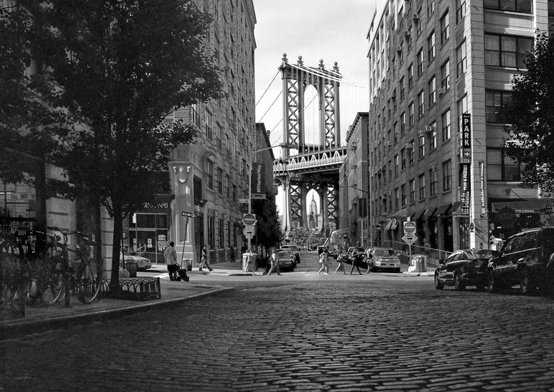 May include: A black and white photo of a street in New York City with the Manhattan Bridge in the background. The street is lined with brick buildings and there are people walking on the sidewalk.