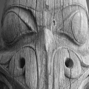 May include: Close-up of a weathered wooden carving of a face with large eyes, a prominent nose, and a wide mouth.