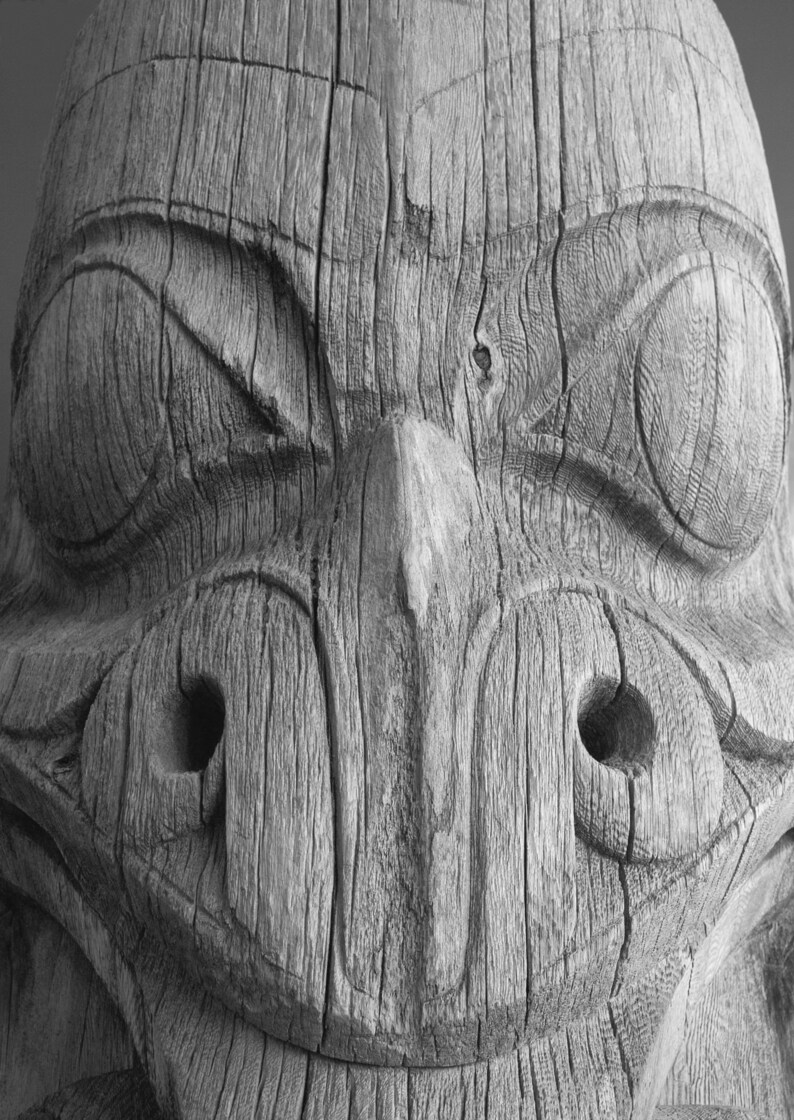 May include: Close-up of a weathered wooden carving of a face with large eyes, a prominent nose, and a wide mouth.