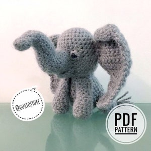 Könnte beinhalten: Ein gehäkeltes graues Elefanten-Spielzeug mit großen Ohren und einem nach oben gerichteten Rüssel. Der Elefant sitzt auf einer reflektierenden Oberfläche. Das Bild enthält den Text "PDF PATTERN" und den Instagram-Handle "@guatostore".