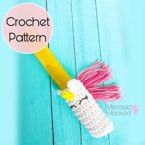May include: Crochet pattern for a unicorn popsicle holder. The holder is white with a yellow horn and pink mane. The text "Mermaid Hooked" is visible in the bottom right corner.