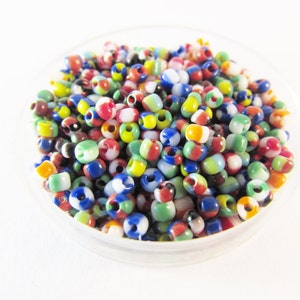 Può includere: Primo piano di una piccola ciotola piena di perline di vetro colorate. Le perline sono un mix di rosso, verde, blu, giallo, bianco e nero.