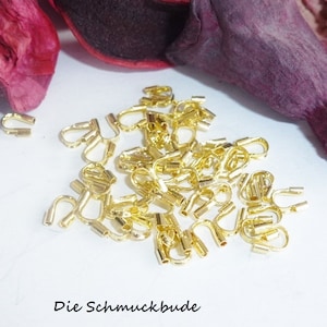 Puede incluir: Un montón de anillos de salto de metal dorado, también conocidos como anillos de conexión, utilizados para la fabricación de joyas. Los anillos son pequeños y tienen una forma redondeada.