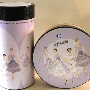 May include: A set of four dessert plates in a round tin box. The box is decorated with a purple and white design featuring five women wearing dresses with ruffles. The text on the box reads "Set of 4 dessert plates".