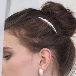 May include: A woman wearing a white lace dress with a pearl hair comb and pearl drop earrings.