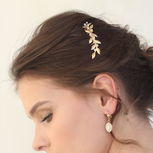 May include: Gold hair comb with a delicate leaf design and small pearl accents. The comb is worn in a woman's hair.