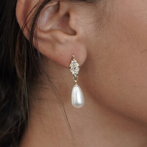 May include: Gold earrings with a small cluster of clear rhinestones and a single white pearl drop.