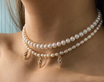 May include: A layered pearl choker necklace with three gold pendant charms featuring clear cubic zirconia stones.