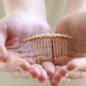 May include: A gold hair comb with pearl accents. The comb is held in the palms of two hands.