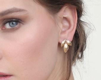 May include: A woman wearing gold leaf earrings and a gold bracelet with a leaf design.