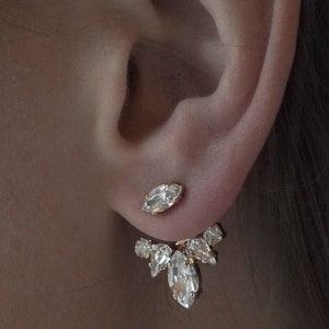 May include: A pair of gold earrings with clear crystal stones. The earrings are designed with a single stone at the top and a cluster of stones dangling below.