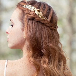 May include: A woman with long, wavy, auburn hair is wearing a gold leaf hair comb. The comb is placed in a braid on the side of her head.