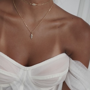 May include: A woman wearing a white off-the-shoulder top with a gold chain necklace and a gold choker necklace with a small diamond-shaped pendant.