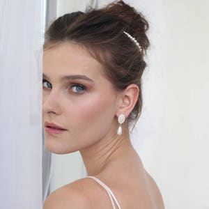 May include: A woman with brown hair wearing a white dress and pearl earrings. She is looking off to the side and has a pearl hair comb in her hair.