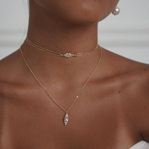 May include: A woman wearing a gold chain necklace with a small diamond pendant and a gold choker necklace with a larger diamond pendant.