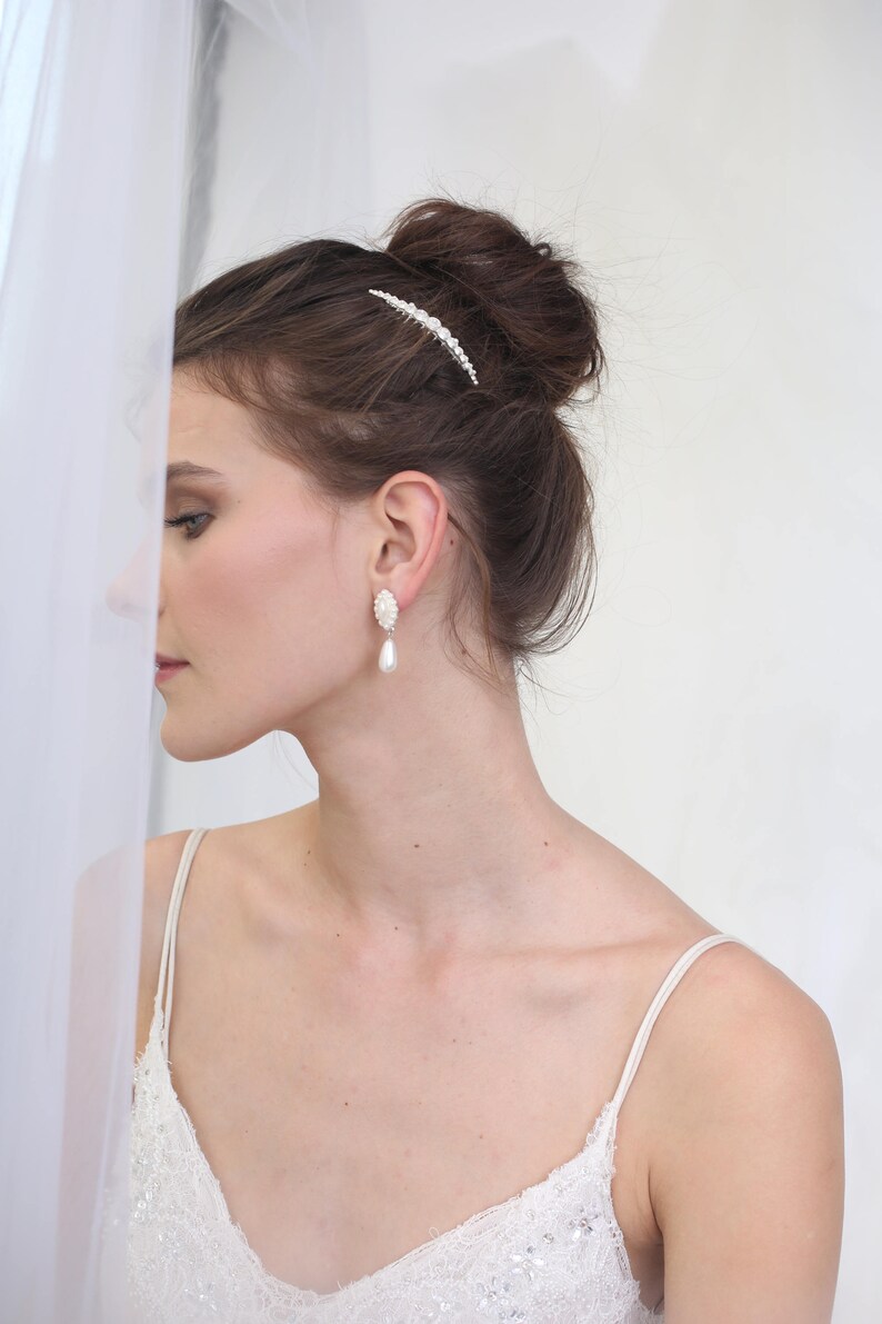 May include: A woman wearing a white lace dress with a pearl hair comb and pearl drop earrings.