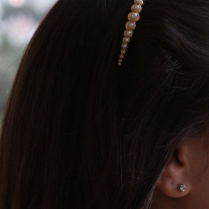 May include: A gold hair clip with a row of faux pearls. The clip is curved and has a subtle shine.