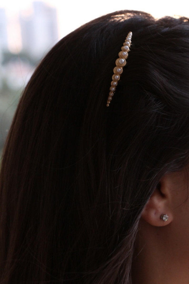 May include: A gold hair clip with a row of faux pearls. The clip is curved and has a subtle shine.