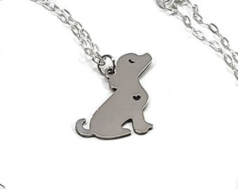 May include: A silver chain necklace with a small silver dog pendant. The dog is sitting with its head tilted up.