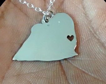 May include: A silver necklace with a heart-shaped pendant. The pendant is in the shape of two people hugging, with a small heart cut out of the pendant.
