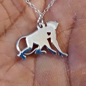 May include: A silver necklace with a monkey pendant. The monkey is holding a heart in its hand.