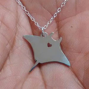 May include: A silver necklace with a manta ray pendant. The pendant has a small heart cut out of it.