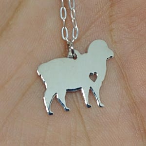 May include: A silver necklace with a sheep silhouette pendant. The pendant has a small heart cutout in the center.