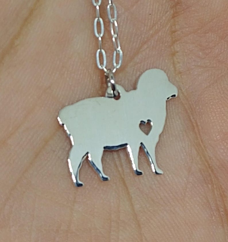 May include: A silver necklace with a sheep silhouette pendant. The pendant has a small heart cutout in the center.