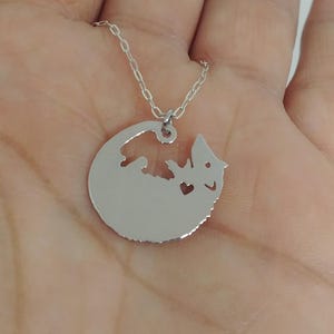 May include: A silver necklace with a round pendant featuring a cut-out silhouette of a lizard with a heart inside.