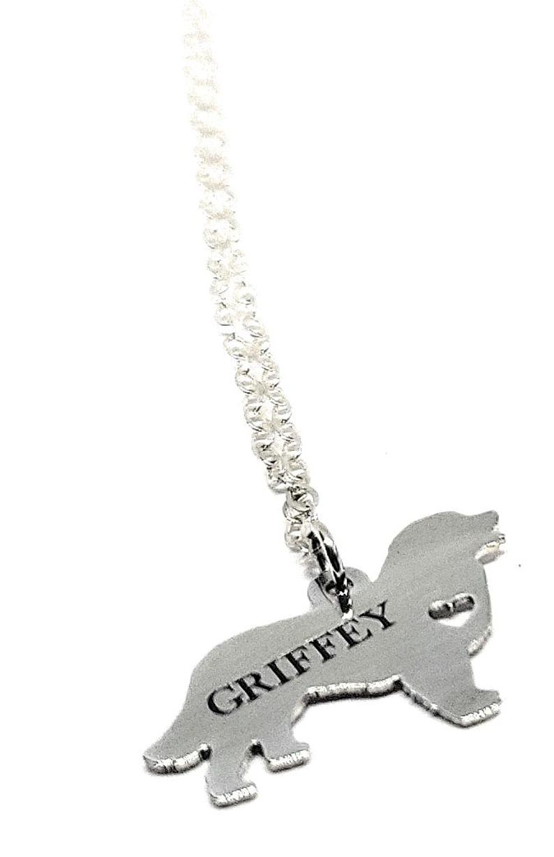 May include: Silver necklace with a dog-shaped pendant. The pendant is engraved with the name "GRIFFEY".