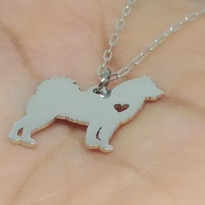 May include: Silver necklace with a small, detailed silhouette of a dog with a heart cutout. The chain is a delicate, silver chain.