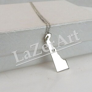 May include: A silver necklace with a pendant shaped like the state of Delaware. The necklace is in a white box with the text "LazerArt" printed on it.