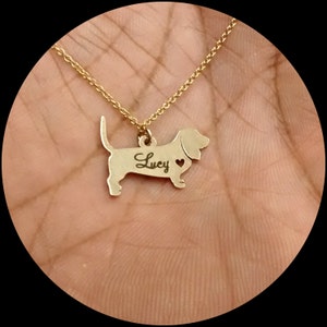 May include: Gold necklace with a dachshund pendant. The pendant has the name "Lucy" engraved on it and a small heart cutout.