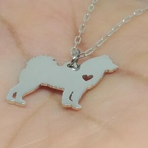 May include: Silver necklace with a small, detailed silhouette of a dog with a heart cutout. The chain is a delicate, silver chain.