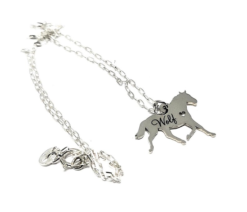 May include: Silver necklace with a horse pendant. The pendant has the word "Wolf" engraved on it and a small heart cutout.