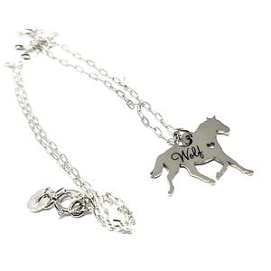 May include: Silver necklace with a horse pendant. The pendant has the word "Wolf" engraved on it and a small heart cutout.