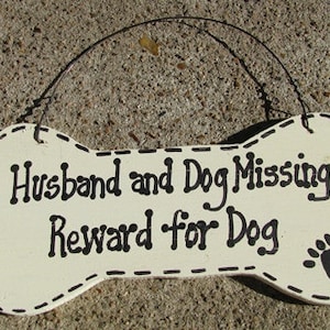 May include: Bone-shaped wooden sign with the text "Husband and Dog Missing! Reward for Dog." The sign is off-white with black text and a paw print. A wire is attached for hanging.