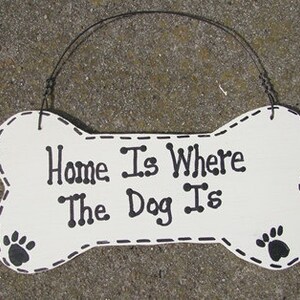May include: White wooden bone-shaped sign with black text that reads "Home Is Where The Dog Is". The sign has black paw prints on each end and a black stitched outline.