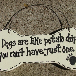 May include: White wooden bone-shaped sign with black text that reads "Dogs are like potato chips you can't have just one." A black paw print is in the lower right corner.