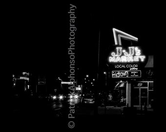 May include: Black and white photo of a storefront with a neon sign that reads "J-J's Market" with the words "Local Color Gallery & Framers" below it. The sign is lit up and the storefront is dark.